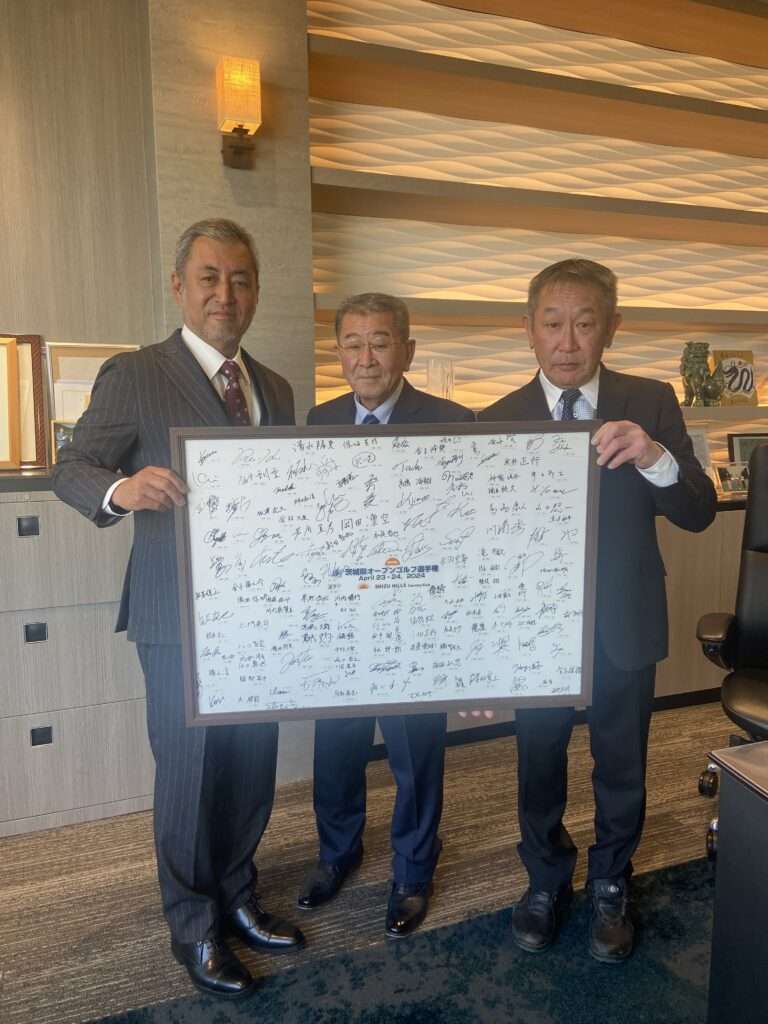 2024年茨城県オープンゴルフ選手権の寄せ書きが入った額縁を掲げるスーツ姿の3人の男性。